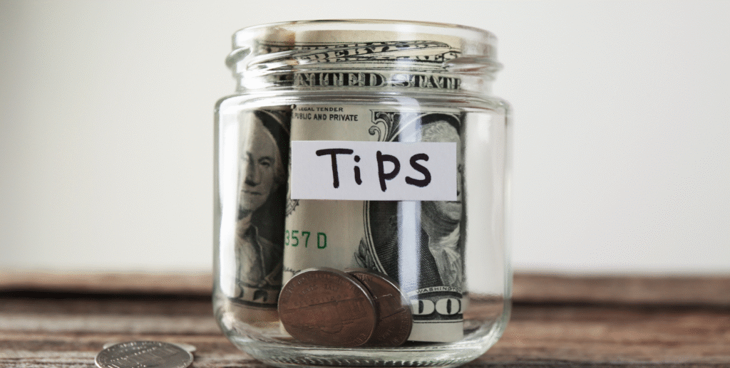 Glas mit Trinkgeld in Scheinen und Münzen, beschriftet mit "Tips"
