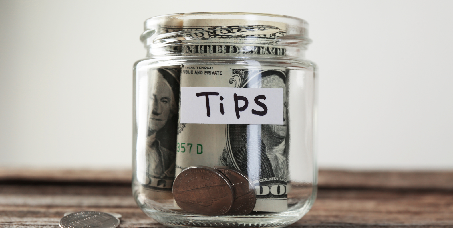 Glas mit Trinkgeld in Scheinen und Münzen, beschriftet mit "Tips"