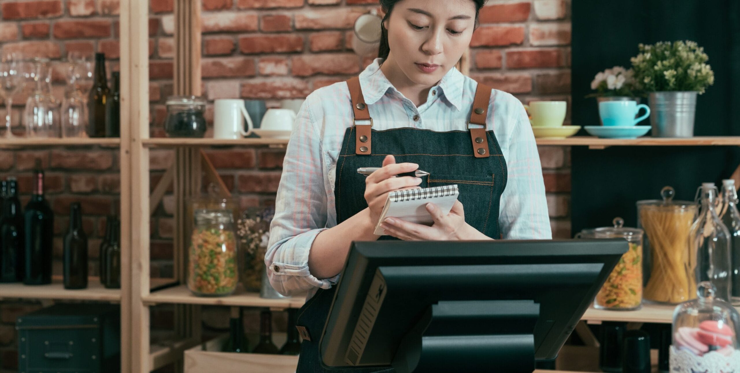 Eine Frau steht an einem Verkaufstresen in einem Restaurant hinter einer Kasse.