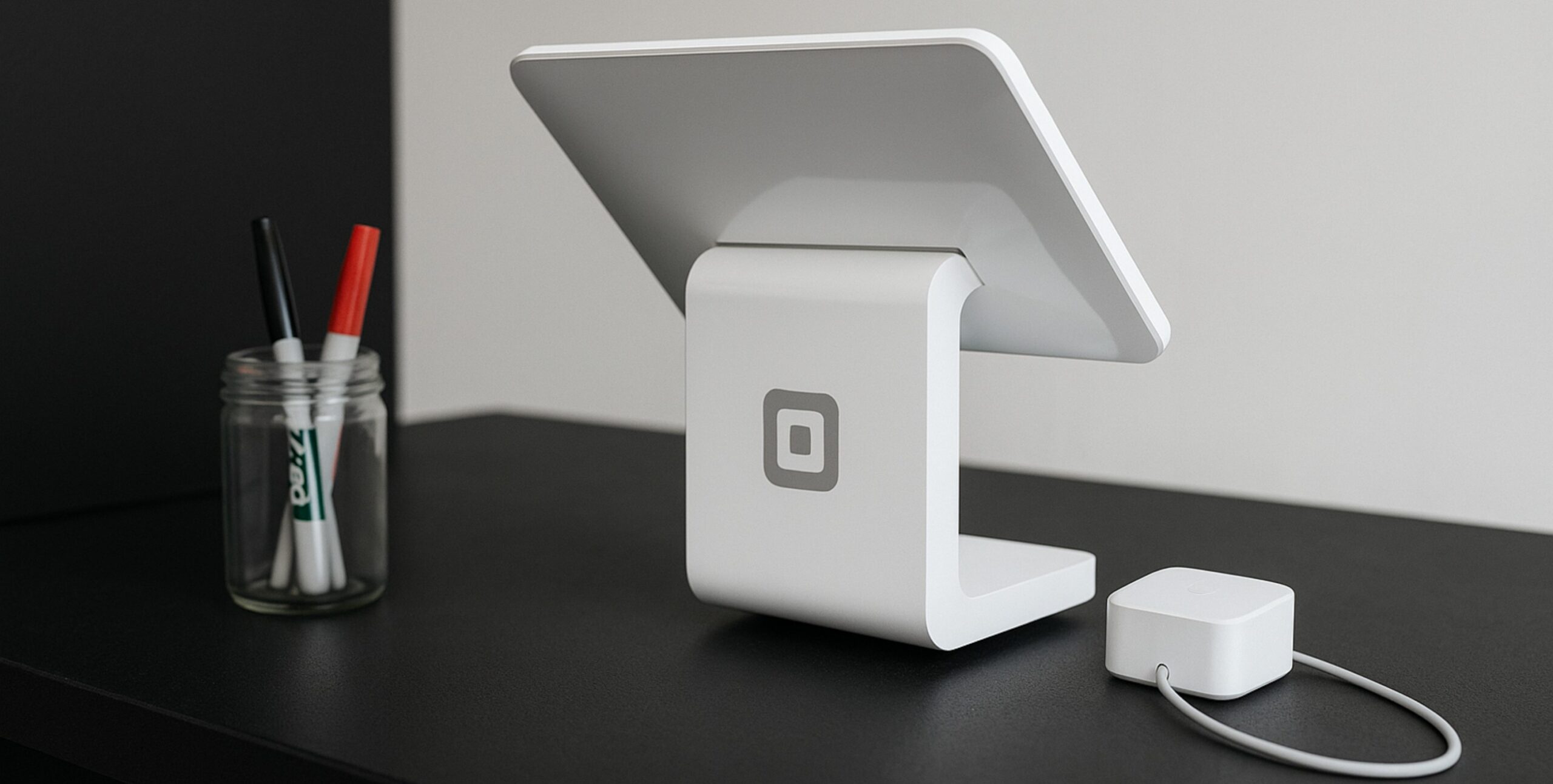 Eine digitale Tablet Kasse steht auf einem schwarzen Schreibtisch, daneben steht ein Glas mit Stiften.